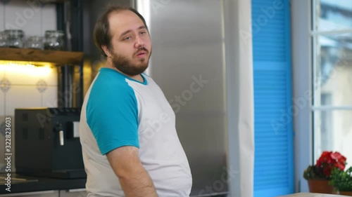Sad and hungry overweight man opening and closing fridge being on healthy diet photo