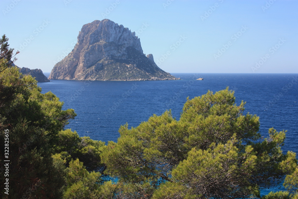 The solitary islet of Es Vedra in contrast against the blue sea of ​​Ibiza immersed in the green and arid wild nature