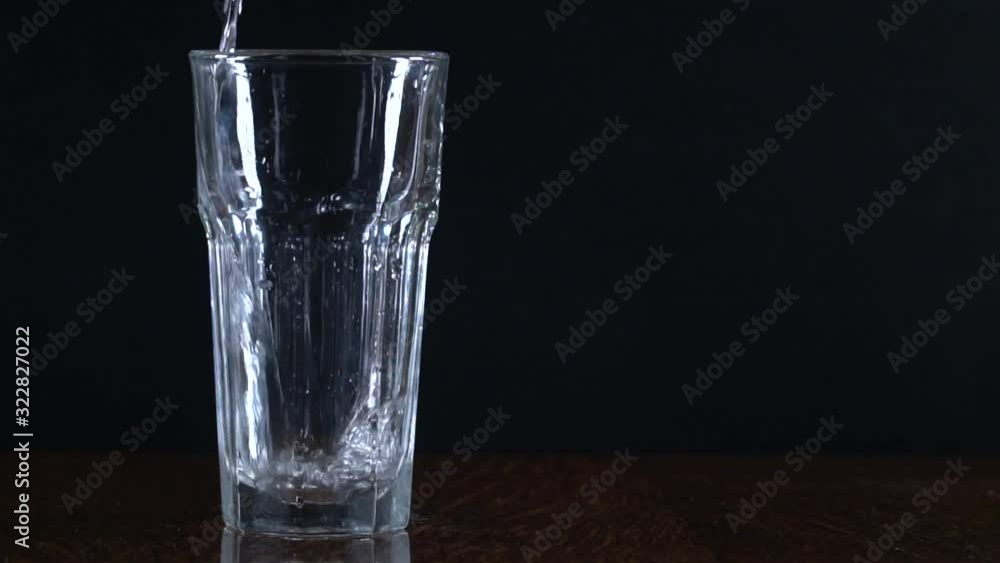Glass on a black background. Pour water into a glass. Transparent container. Pure water. Slow motion. Glass on a black background. Pour water into a glass. Transparent container. Pure water. Slow motion.