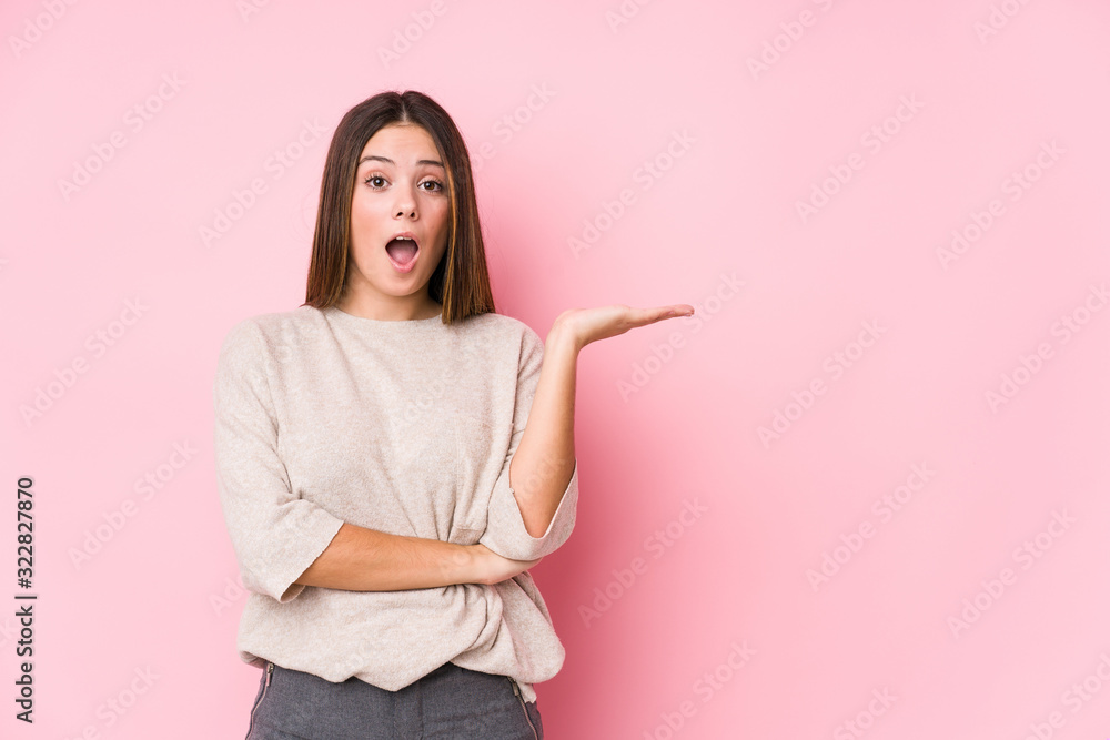 Young caucasian woman posing isolated impressed holding copy space on palm. Young caucasian woman posing isolated impressed holding copy space on palm.