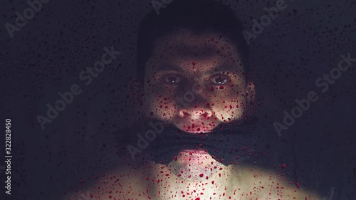 Kidnapped Kid hostage with a tied mouth. Behind a transparent glass covered with bloody drops on a dark background. Ask for help. Close up photo