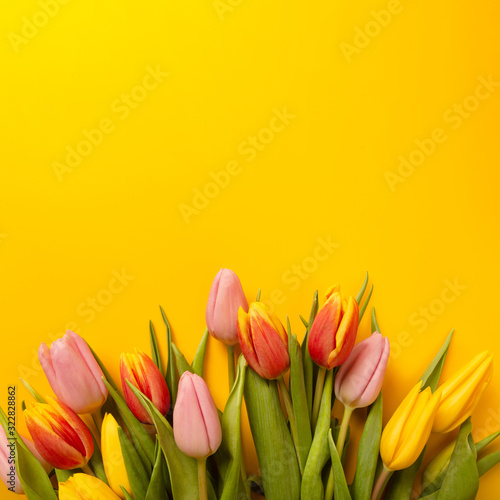 Square background with a bouquet of tulips on an yellow background. Flat lay, top view with copyspace. International Women's Day, spring concept.
