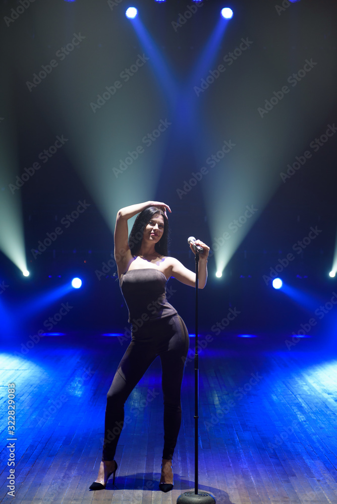 Pop musician with microphone singing a song on the stage in blue light background.