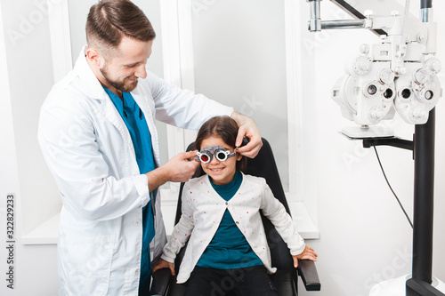 Optometrist doctor putting trial frame on a girl to check eyesight. Vision correction children