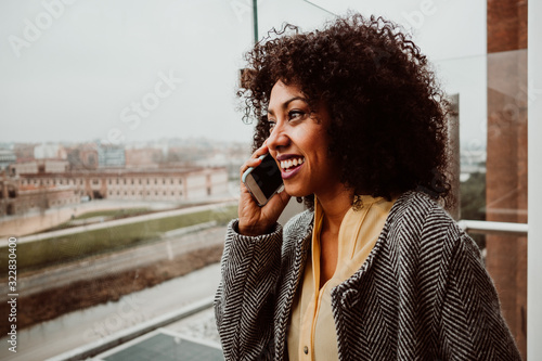 .Pretty young african american woman talking and chatting from her smartphone from a terrace overlooking the city of Madrid. Lifestyle