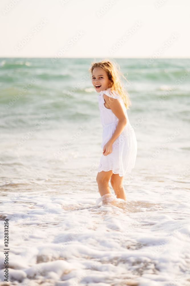 A blonde girl in a white dress standing in the sea knee-deep. waves at sea A blonde girl in a white dress standing in the sea knee-deep. waves at sea