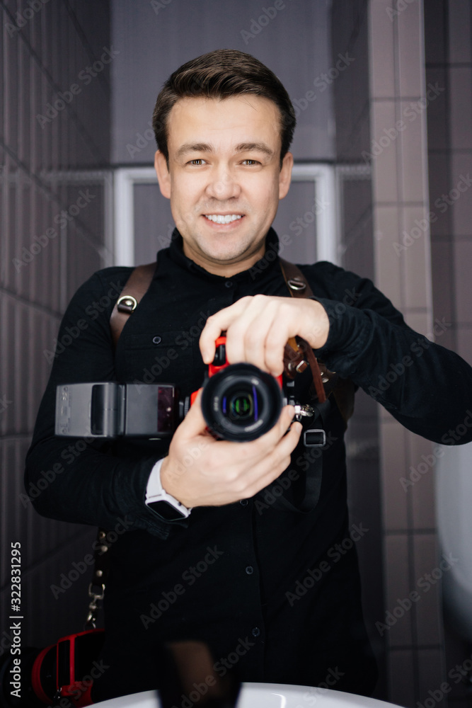 Photographer in black clothes taking a selfie with the camera in the mirror and smiling Photographer in black clothes taking a selfie with the camera in the mirror and smiling