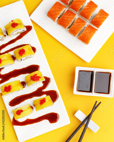Sushi rolls on white ceramic plates on a yellow background. A look from above. photo