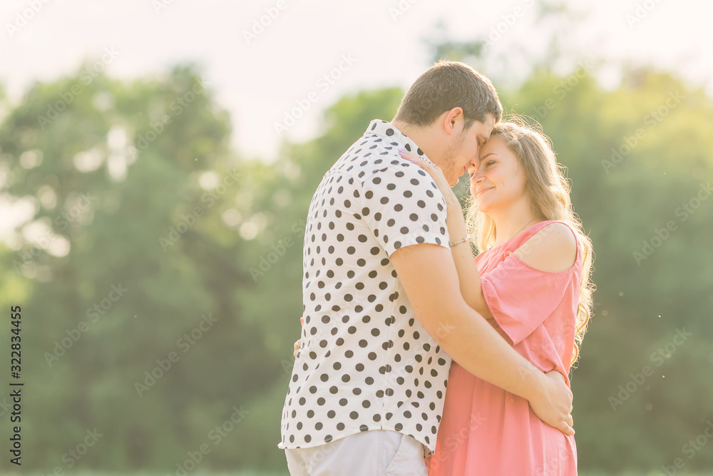 husband gently hugs his pregnant wife in a pink dress. couple in husband gently hugs his pregnant wife in a pink dress. couple in