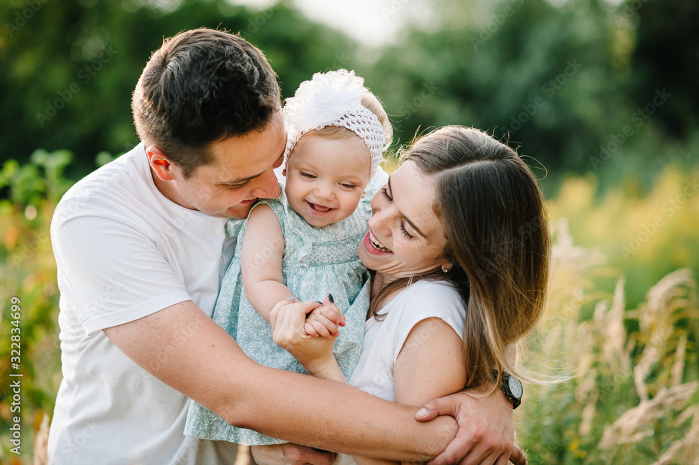 The daughter hugging parents on nature. Mom, dad and girl toddler, walk in the grass. Happy young family spending time together, outside, on vacation, outdoors. The concept of family holiday. The daughter hugging parents on nature. Mom, dad and girl toddler, walk in the grass. Happy young family spending time together, outside, on vacation, outdoors. The concept of family holiday.