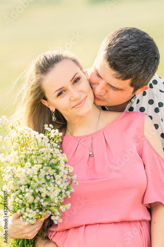 pregnant woman holds bouquet of flowers and man kisses her. clos