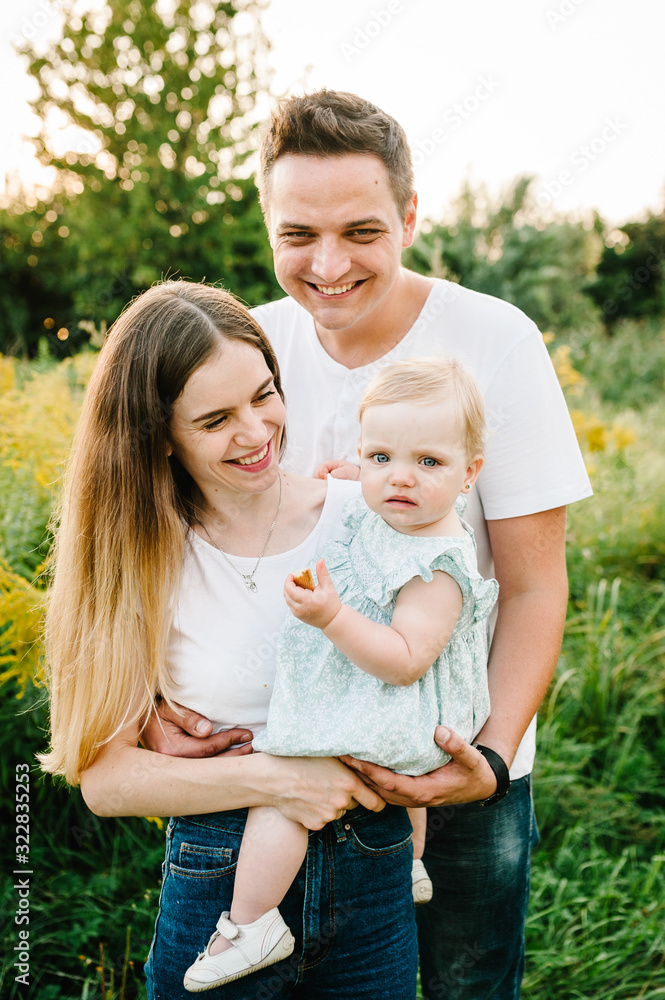 The daughter hugging parents on nature. Mom, dad and girl toddler, walk in the grass. Happy young family spending time together, outside, on vacation, outdoors. The concept of family holiday. The daughter hugging parents on nature. Mom, dad and girl toddler, walk in the grass. Happy young family spending time together, outside, on vacation, outdoors. The concept of family holiday.