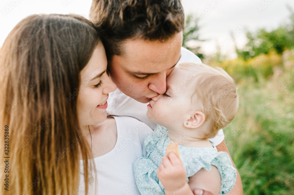 Portrait of a happy young family spending time together on nature, on vacation, outdoors. Mom, dad holds daughter stand on the grass. The concept of family holiday. Portrait of a happy young family spending time together on nature, on vacation, outdoors. Mom, dad holds daughter stand on the grass. The concept of family holiday.