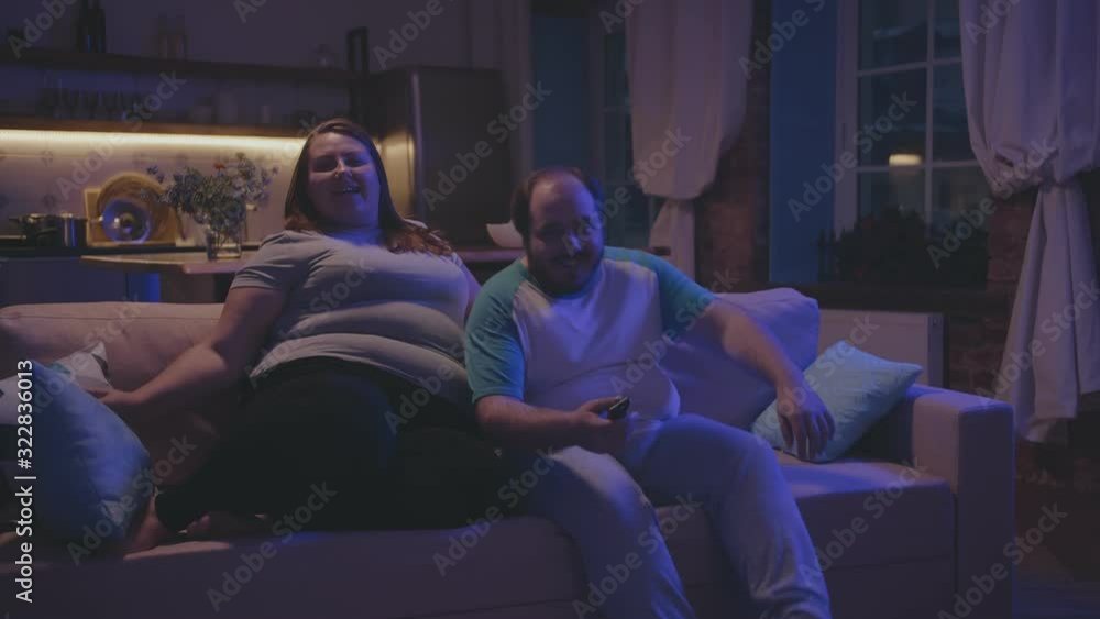 Overweight lazy couple watching tv at home in evening Overweight lazy couple watching tv at home in evening