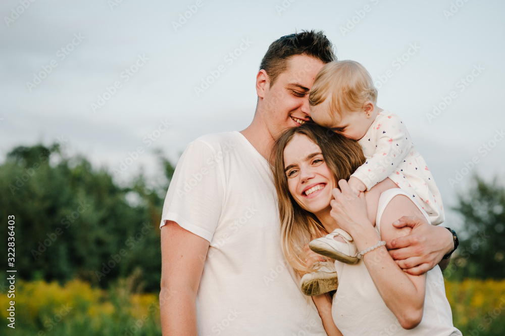 The daughter hugging parents on nature. Mom, dad and girl toddler, walk in the grass. Happy young family spending time together, outside, on vacation, outdoors. The concept of family holiday. The daughter hugging parents on nature. Mom, dad and girl toddler, walk in the grass. Happy young family spending time together, outside, on vacation, outdoors. The concept of family holiday.