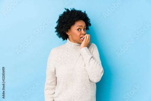 Middle aged african american woman against a blue background isolated biting fingernails, nervous and very anxious. photo