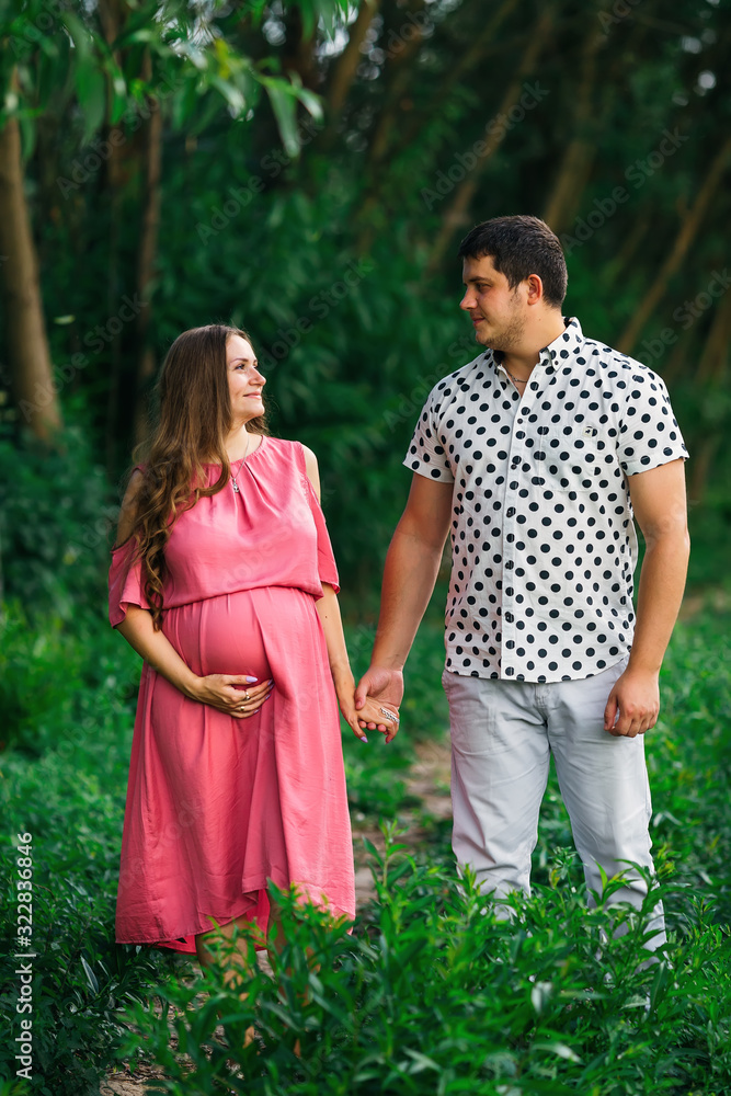pregnant woman in a pink dress gently touches her tummy and a ma