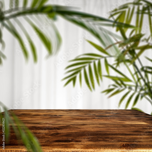 Brown wooden table and white background with green leaves. 