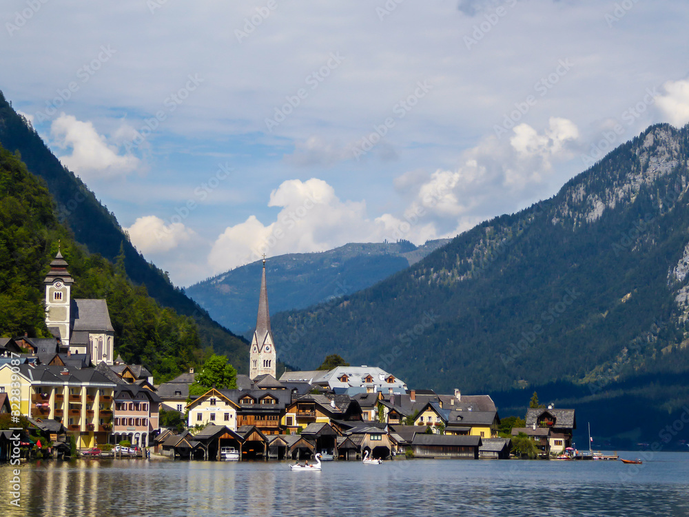 An idyllic small village located by the lake in Hallstatt, Austria. There is a tall church tower in the middle of the village. Alpine village. Idyllic landscape. High mountains rising from the lake.