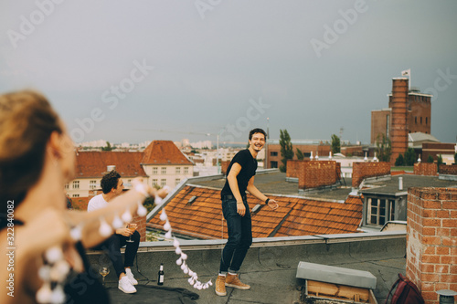 Cheerful man and woman playing with string light on terrace during rooftop party photo