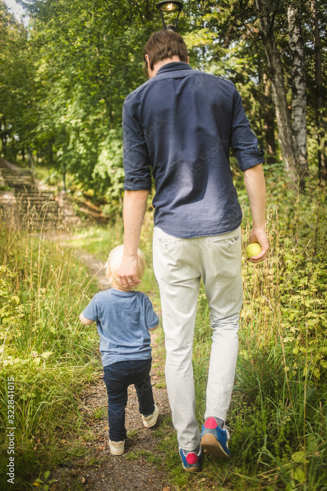 Full length rear view of father and son walking amidst plants at park Full length rear view of father and son walking amidst plants at park