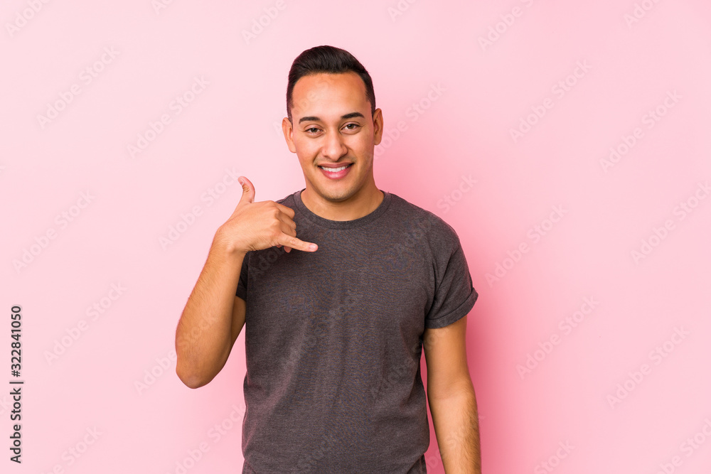 Yooung latin man posing in a pink backgroundshowing a mobile phone call gesture with fingers. Yooung latin man posing in a pink backgroundshowing a mobile phone call gesture with fingers.