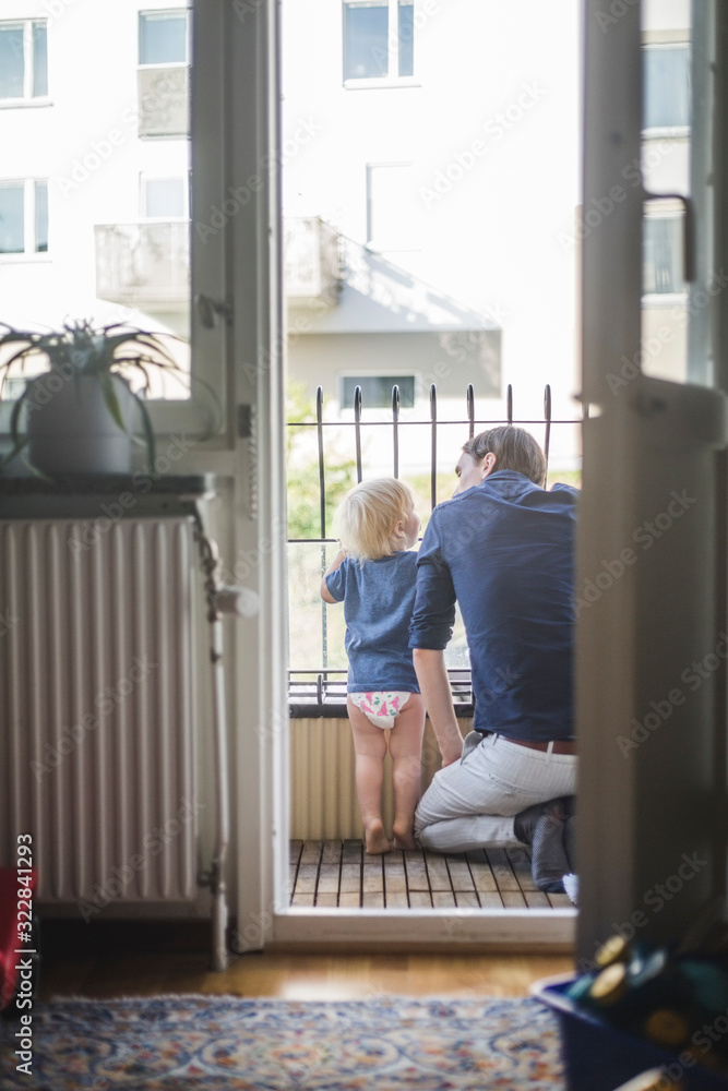 Rear view of man kneeling by son in balcony seen through doorway Rear view of man kneeling by son in balcony seen through doorway