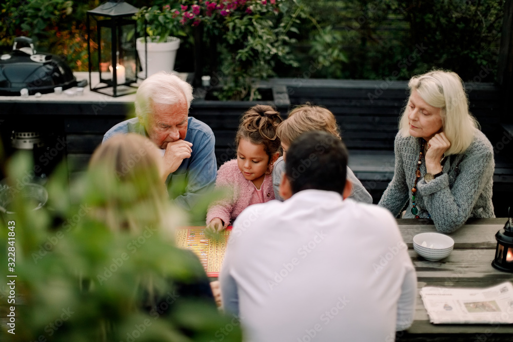 Multi-generation family playing board game on table while sitting in patio Multi-generation family playing board game on table while sitting in patio
