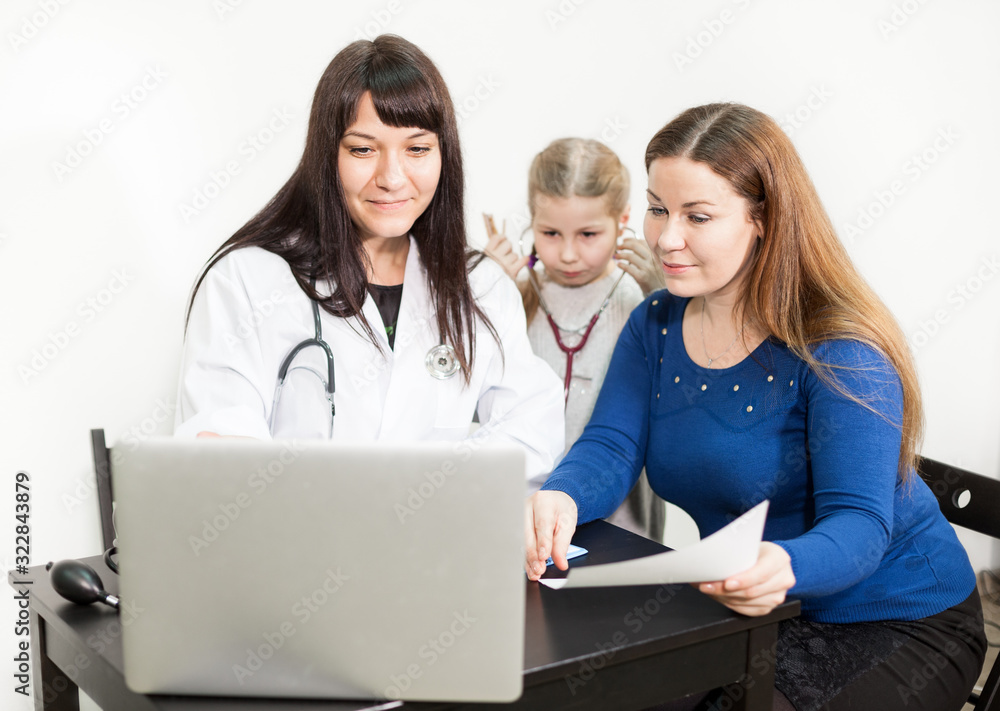 Doctor and mother looking at laptop screen and talking about young child treatment Doctor and mother looking at laptop screen and talking about young child treatment