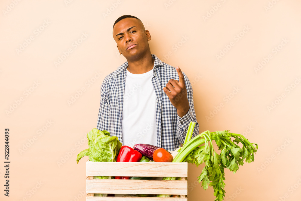 Young farmer man isolated on a beige background pointing with finger at you as if inviting come closer. Young farmer man isolated on a beige background pointing with finger at you as if inviting come closer.