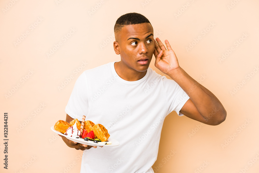 Young latin man holding a waffle isolated trying to listening a gossip. Young latin man holding a waffle isolated trying to listening a gossip.