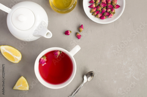 Herbal tea with pink roses in the white cup on the grey concrete background. Top view. Copy space.
