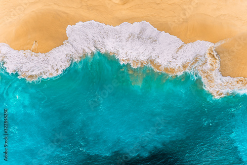 Fototapeta Naklejka Na Ścianę i Meble -  Aerial view of turquoise ocean waves in Kelingking beach, Nusa penida Island in Bali, Indonesia. Beautiful sandy beach with turquoise sea. Splashing ocean waves reach sandy beach. Beaches of Indonesia