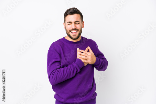 Young caucasian man against a white background isolated laughing keeping hands on heart, concept of happiness.