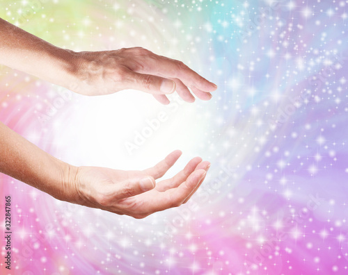 Creating a Healing Rainbow Energy Vortex from White Light - female cupped hands with a spiralling rainbow coloured sparkling background and a ball of white light plus copy space 