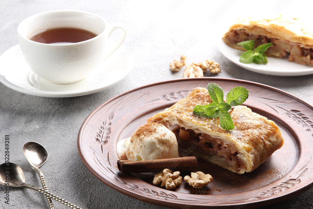 Concept of German cuisine. Apple strudel with cinnamon, nuts and ice cream with a cup of tea on a light background. Background image, copy space Concept of German cuisine. Apple strudel with cinnamon, nuts and ice cream with a cup of tea on a light background. Background image, copy space