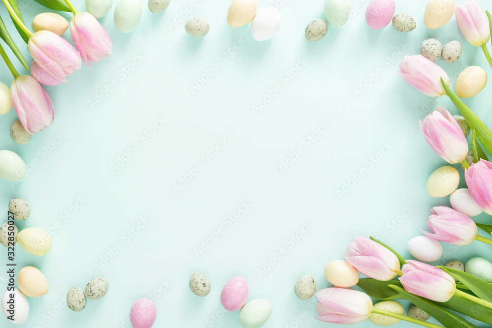 Colored Easter candy eggs and pink tulips on turquoise background. Easter frame.