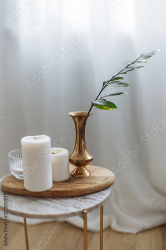 Gold vase with garnish with greens candles marble backsplash wooden board white drapes in cozy scandinavian interior