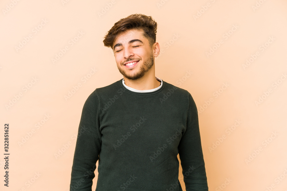 Young arabian man isolated on a beige background laughs and closes eyes, feels relaxed and happy. Young arabian man isolated on a beige background laughs and closes eyes, feels relaxed and happy.