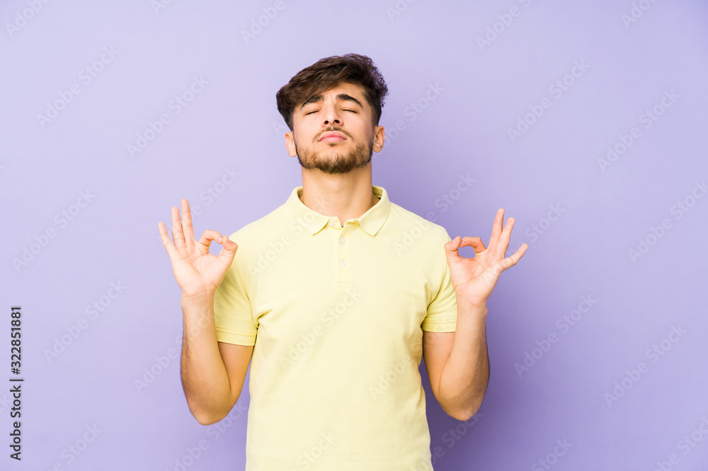 Young arabian man isolated on a purple background relaxes after hard working day, she is performing yoga. Young arabian man isolated on a purple background relaxes after hard working day, she is performing yoga.