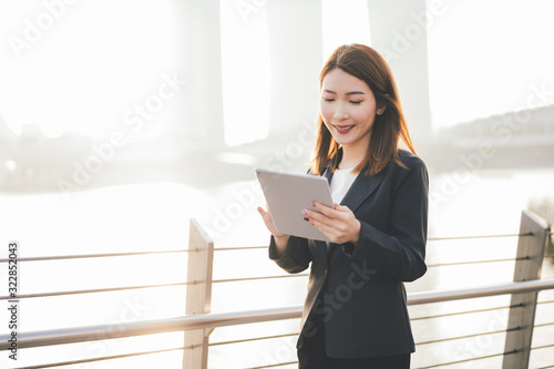 Canvas Print Young Asian business woman with Digital Tablet standing outdoors in modern city financial district