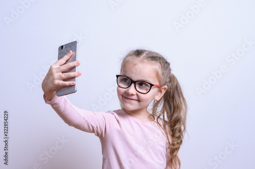 Portrait of a little white girl make selfie on a mobile phone on a gray background