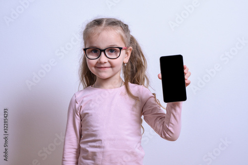 Portrait of a little white girl points to the phone on a gray background