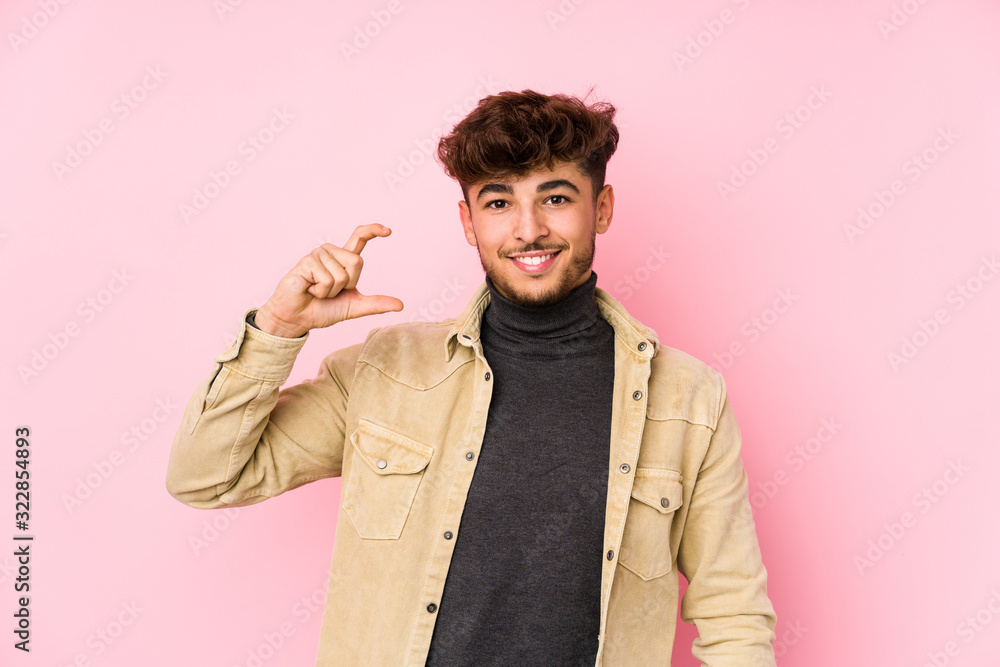 Young arabian man posing in a background isolated holding something little with forefingers, smiling and confident. Young arabian man posing in a background isolated holding something little with forefingers, smiling and confident.