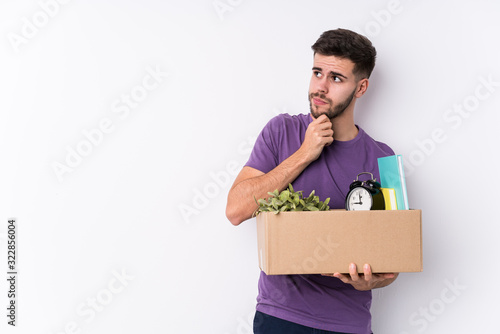 Young caucasian man moving a new home isolated looking sideways with doubtful and skeptical expression.