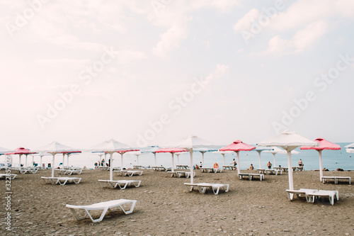 white sunbeds with colorful umbrellas on a pebble beach in the summer
