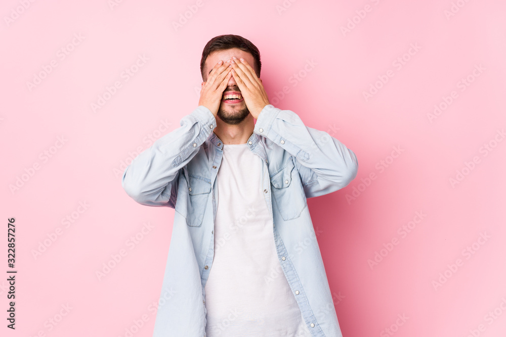 Young caucasian business man posing in a white background isolated covers eyes with hands, smiles broadly waiting for a surprise.< mixto > Young caucasian business man posing in a white background isolated covers eyes with hands, smiles broadly waiting for a surprise.< mixto >