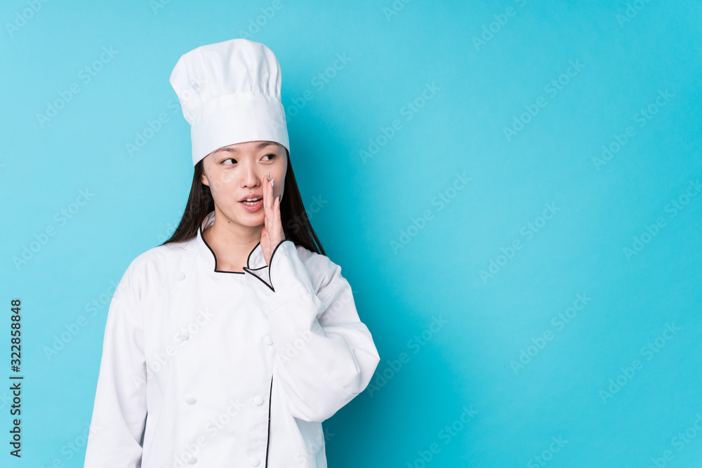 Young chinese chef woman isolated is saying a secret hot braking news and looking aside Young chinese chef woman isolated is saying a secret hot braking news and looking aside