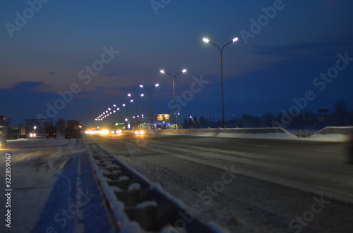 Winter night road at the entrance to the city. The lights of the lampposts and the headlights of cars. It's snowing. Selective focus.  A blur of lights. © Ирина Кусова
