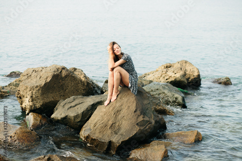 a young beautiful girl in a dress on large stones, a picturesque place on the sea coast